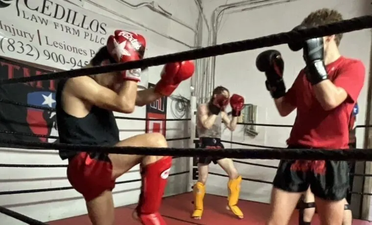 Two students sparring in the ring with a coach watching